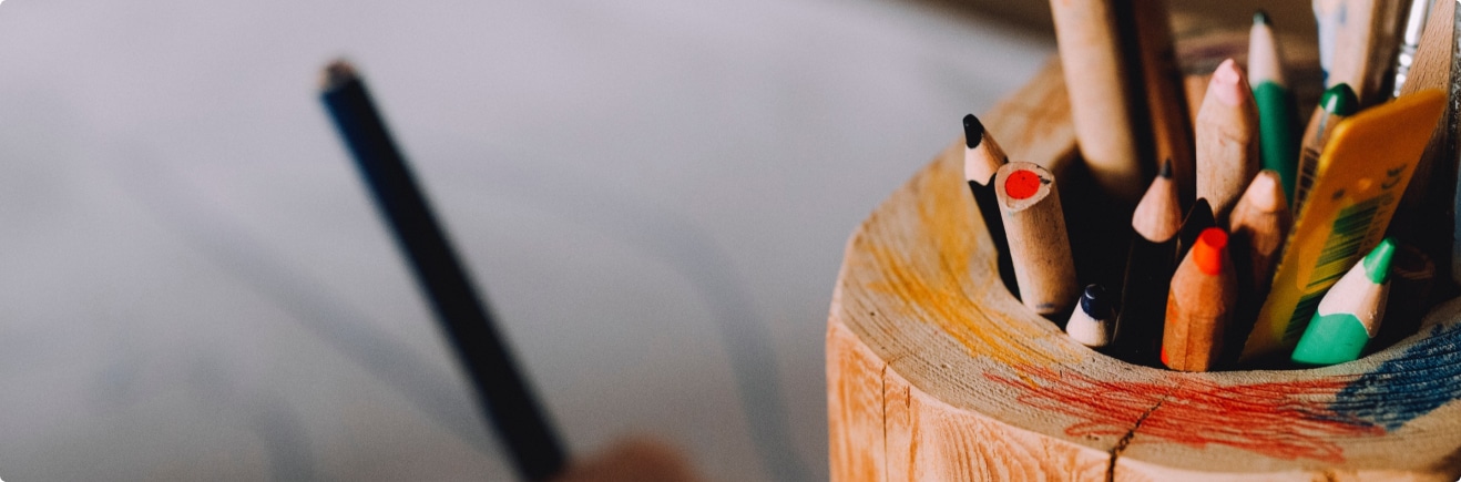 A wooden pencil holder with colored pencils in it.