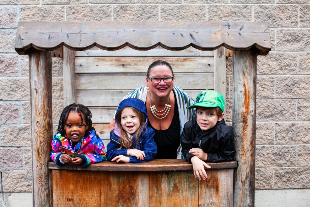 Teacher and three preschool students standing in a wooden play structure