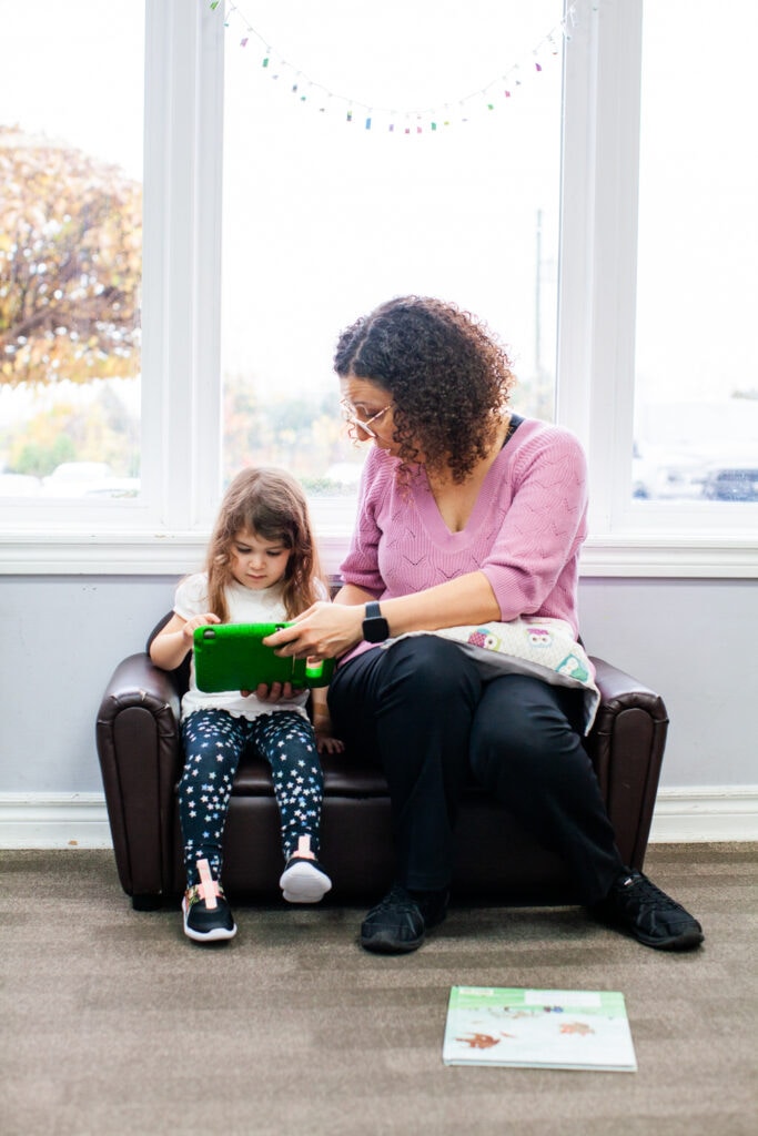 Child using tablet held by adult while they're sitting on a couch