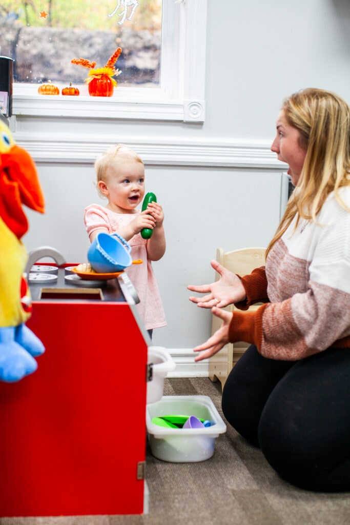 Happy infant shows toy cucumber to surprised adult
