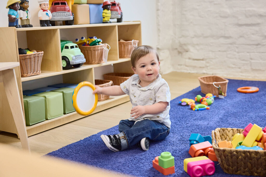 Infant/Toddler aged child sitting on the ground with a number of toys surrounding them
