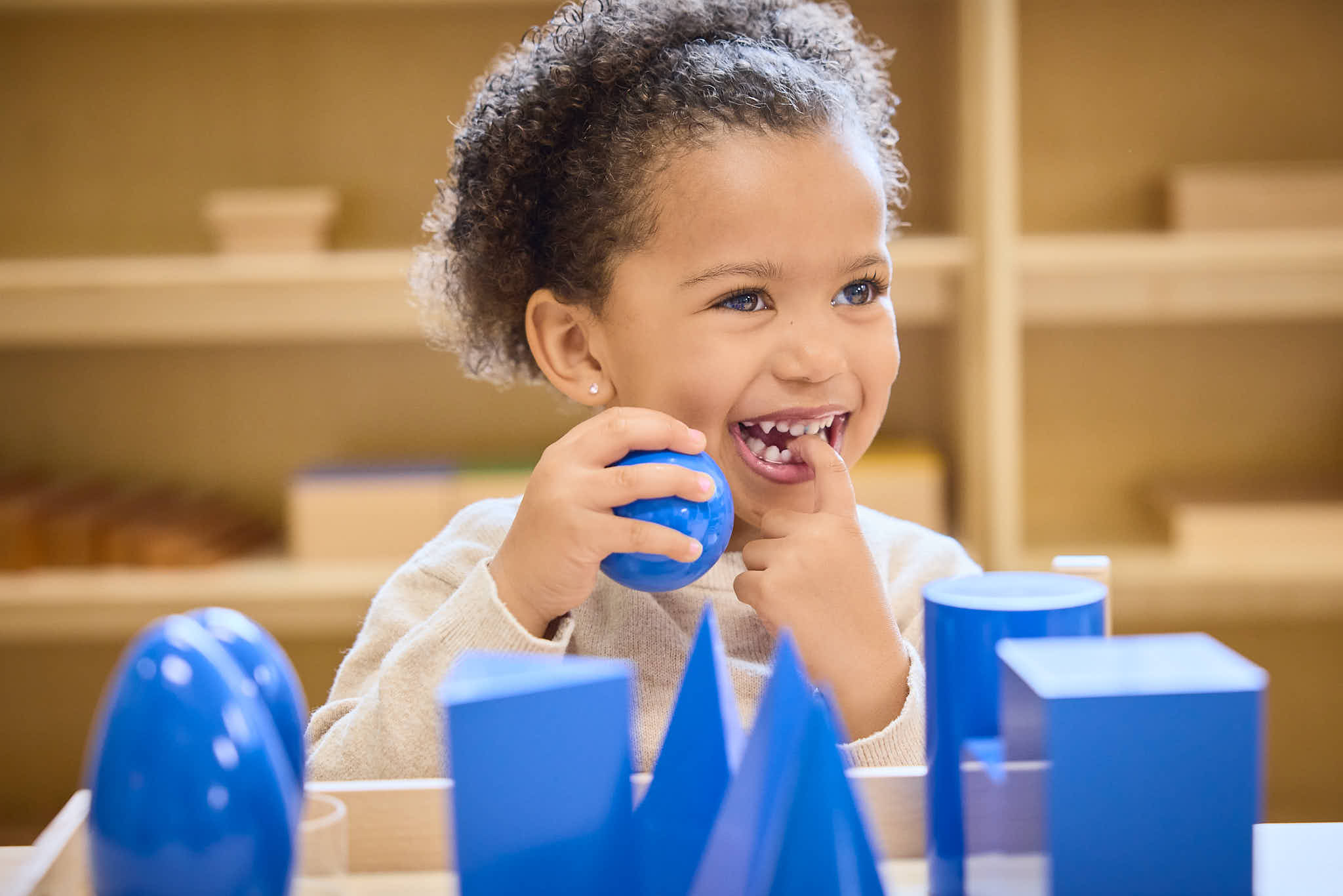 Preschool child interacting with blue Montessori materials and smiling off to the right