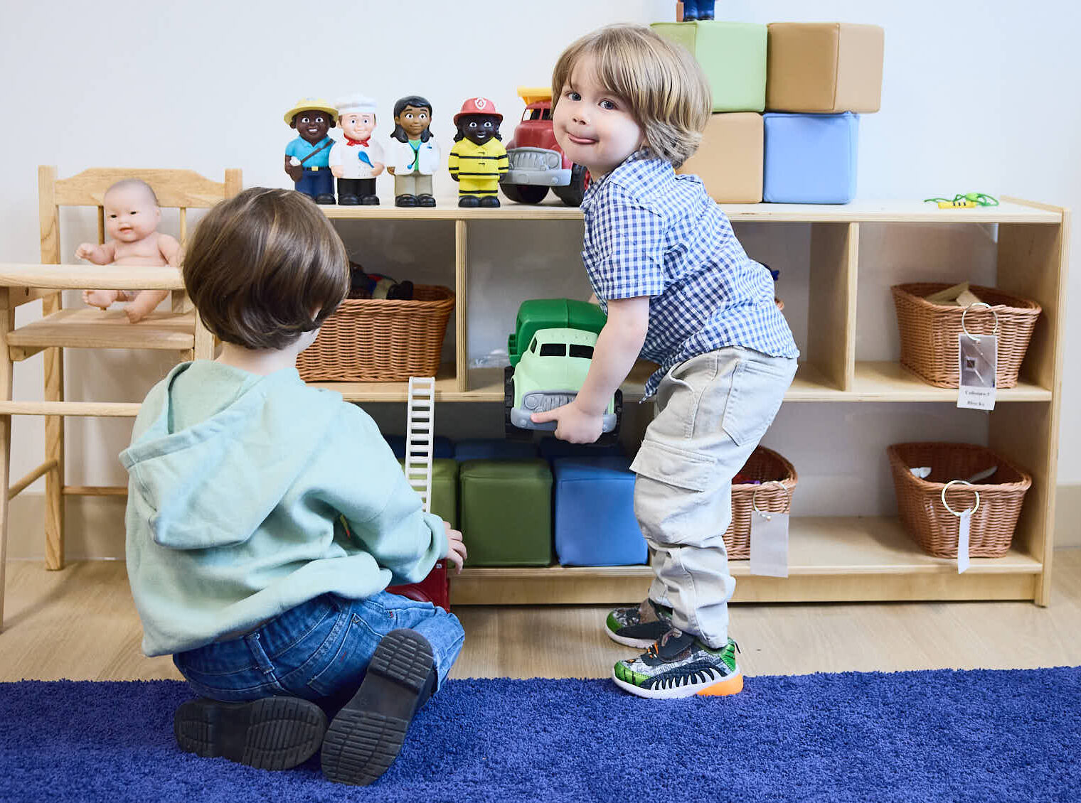 Two boys helping each other as they put toys back onto the shelf