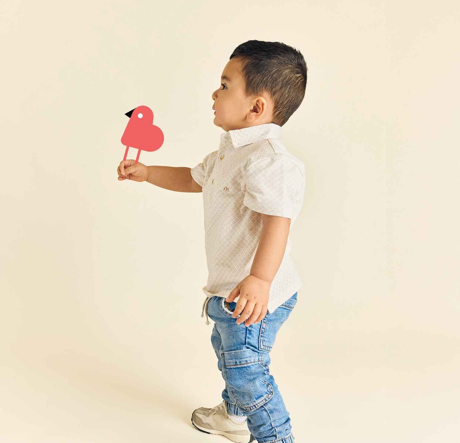 A 2 to 4 year old little boy facing sideways, holding The Learning Nest daycare's logo of a bird