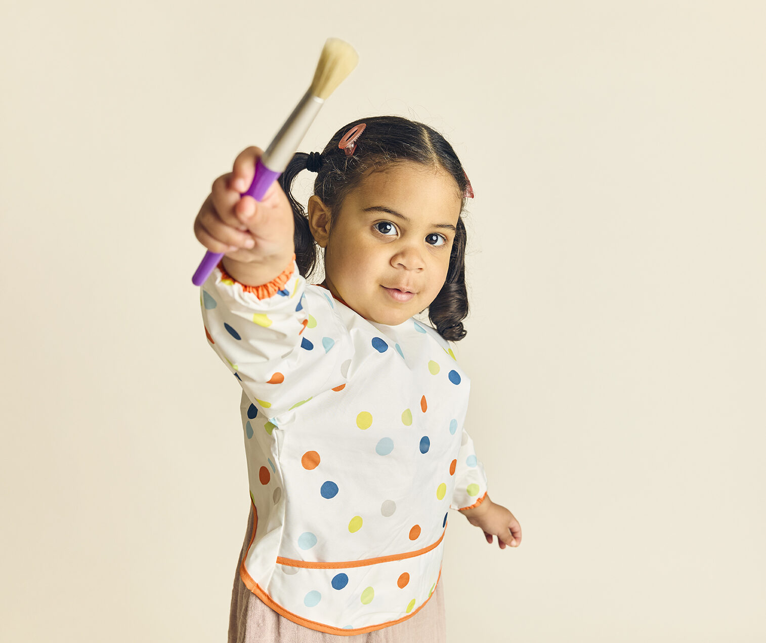 Little girl holding a paintbrush, engaged in STEM activities during enrichment programs at The Learning Nest