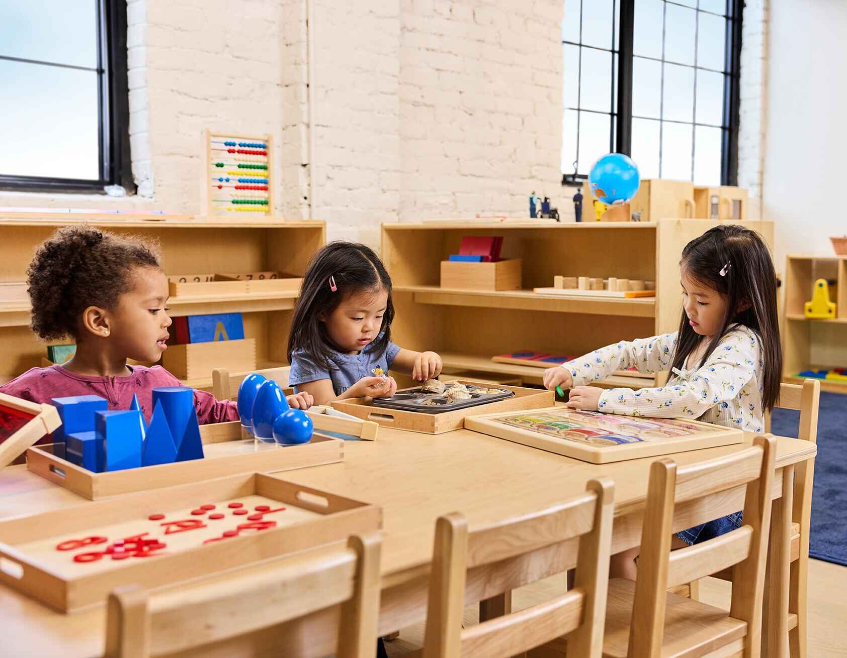 A group of three girls sitting on a wooden table, participating in interactive activities at The Learning Nest daycare.