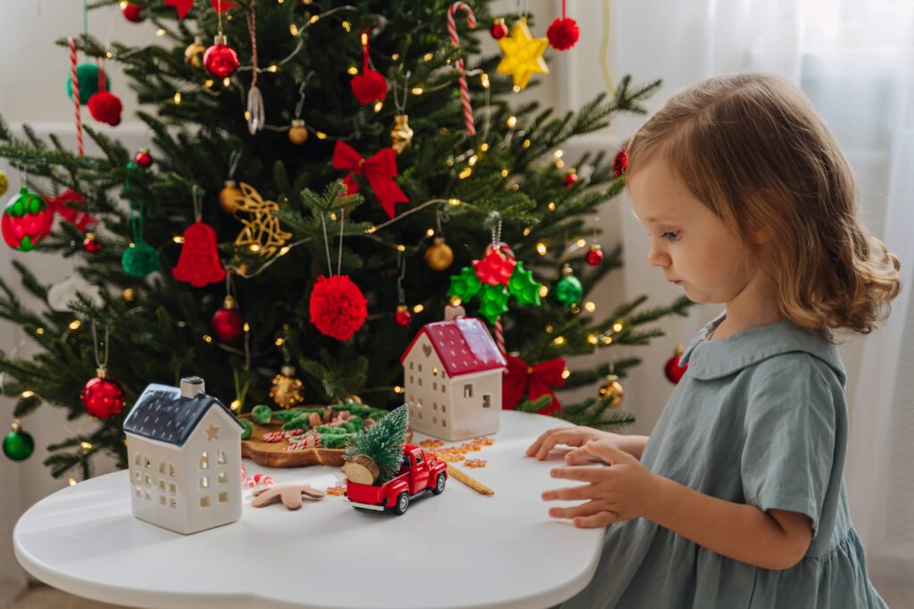 Christmas holidays. A little girl plays with toy cars, little houses and christmas decorations. Holiday Activity for Kids. Merry Christmas and Happy Holidays!